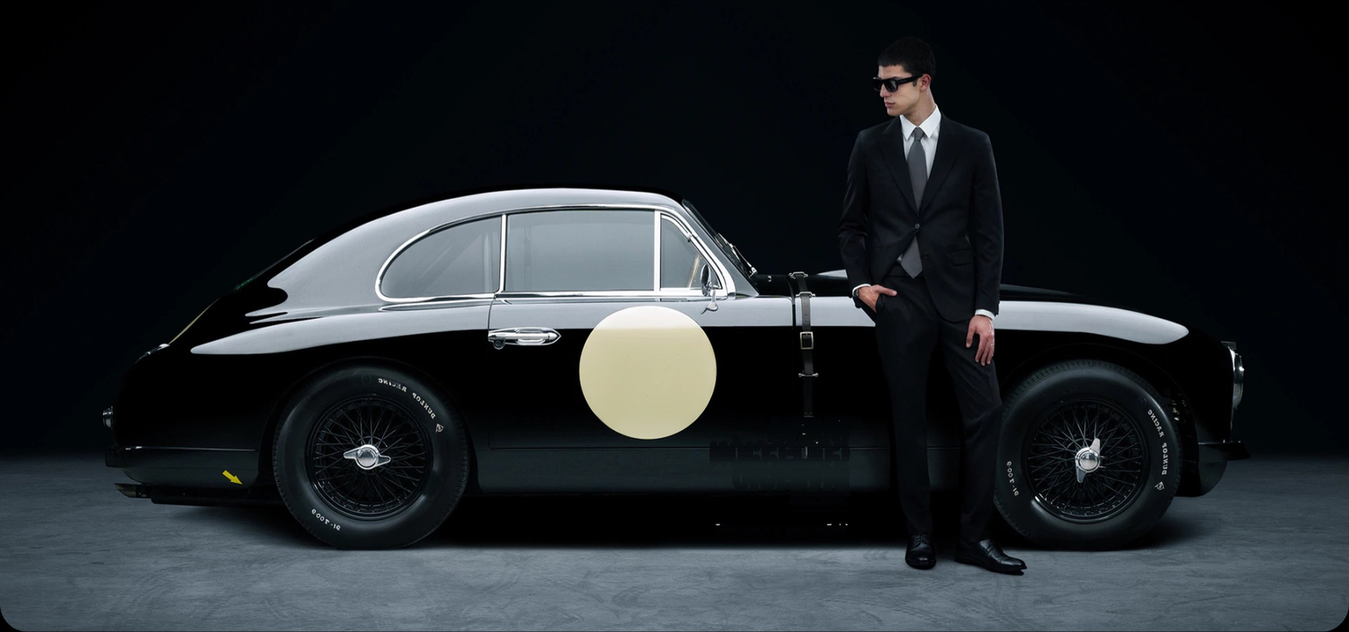 Man in a suit standing next to a vintage car with a black background